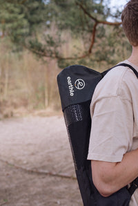 Quelqu'un porte le tapis de yoga de mise à la terre Earthle dans son sac sur le dos, dehors dans la forêt